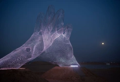 Main géante en maille métallique illuminée la nuit sur le plateau de Gizeh à Forever Is Now 2026