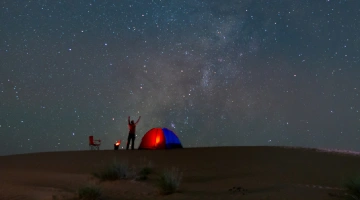 Persona acampando bajo la Vía Láctea en el desierto.
