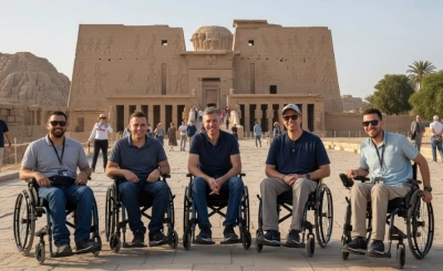   Five wheelchair users smile in front of the Temple of Horus at Edfu, framed by ancient carvings and clear skies—celebrating accessible tourism at a historic Egyptian site.
