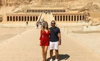 Two tourists standing on the stone pathway leading to Hatshepsut’s Temple, framed by desert cliffs and colonnaded terraces.