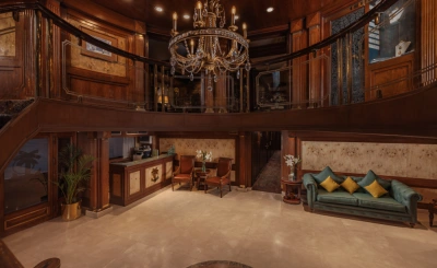 Elegant cruise lobby with a grand chandelier, wood-paneled walls, ornate balcony, and plush seating areas featuring red chairs and a teal tufted sofa.