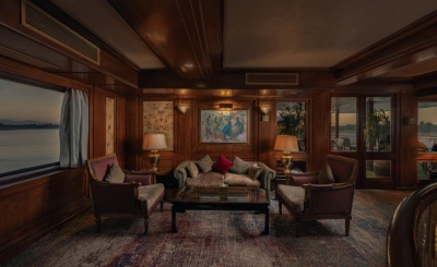 Luxurious lounge with velvet armchairs, gold-accented lamps, and a large window overlooking serene waters.