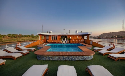 Upper deck of river cruise ship M.S. SALACIA at sunset, featuring a central pool, lounge chairs, and scenic views of greenery and rocky hills.