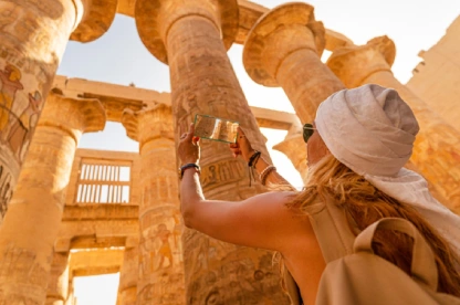 Una turista camina entre los pilares de la Gran Sala Hipóstila del Templo de Karnak y toma fotografías con su teléfono