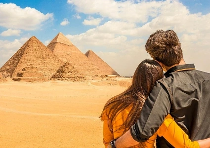 Couple embracing as they admire the Pyramids of Giza under a partly cloudy desert sky.