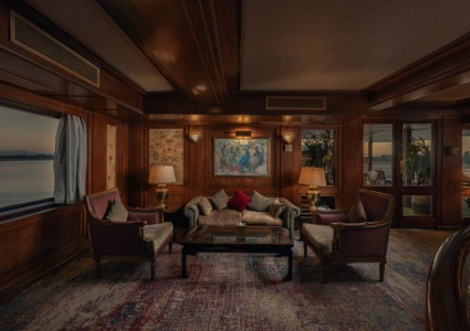 Luxurious lounge with velvet armchairs, gold-accented lamps, and a large window overlooking serene waters.