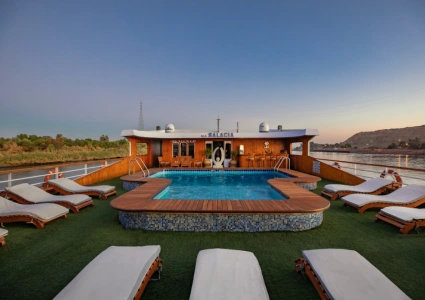 Upper deck of river cruise ship M.S. SALACIA at sunset, featuring a central pool, lounge chairs, and scenic views of greenery and rocky hills.