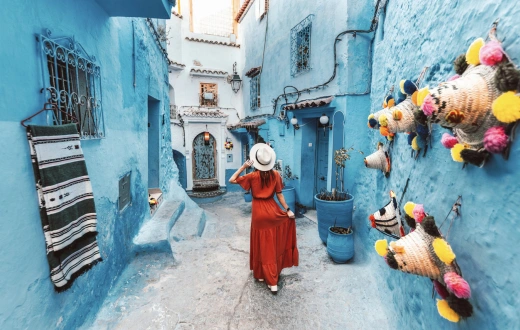 Young woman with red dress visiting the blue city Chefchaouen, Marocco - Happy tourist walking in Moroccan city street - Travel and vacation lifestyle concept