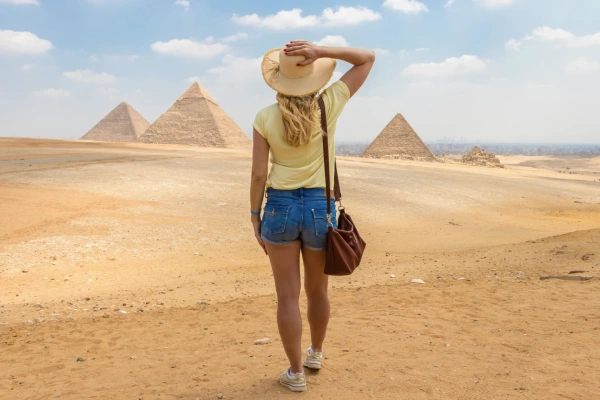 Una donna osserva le Piramidi di Giza nel deserto, simbolo del desiderio di viaggiare sicuri in Egitto.