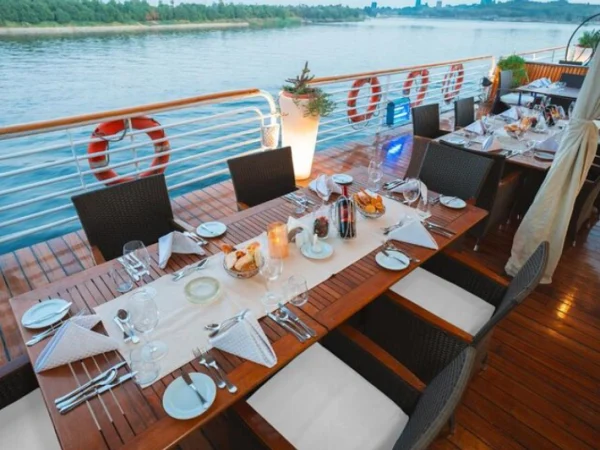 Festlich gedeckte Tafel auf dem Holzdeck eines Nilschiffs mit Blick auf den Nil