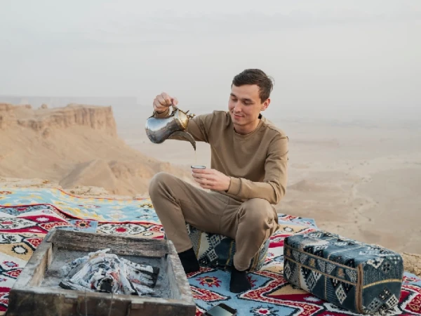 Mann schenkt arabischen Kaffee auf einem Teppich in der Wüste ein