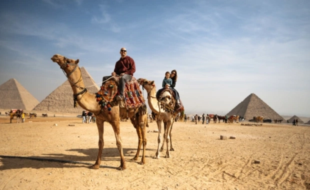 Tourist family riding camels in a vast desert landscape under a clear blue sky, Egypt Cairo to Luxor