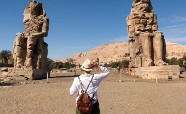 Turista interesada en la egiptología y la arqueología junto a los Colosos de Memnón, las estatuas del faraón Amenhotep III en Luxor, Viaje a Egipto Todo Incluido