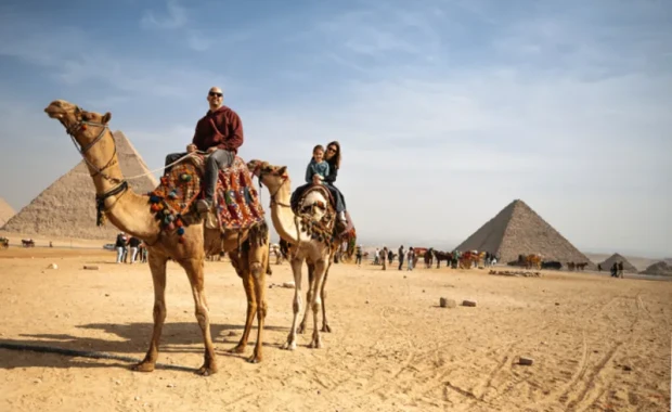 Familia de turistas montando en camello en un amplio paisaje desértico bajo un cielo azul despejado, Tour Egipto