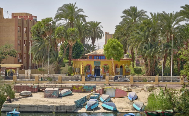 Bateaux colorés au bord du Nil, avec un bâtiment jaune et des palmiers en Égypte, Circuit égypte 10 jours