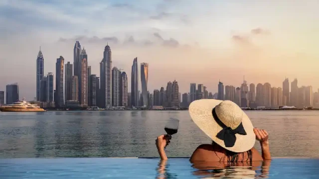 donna con cappello in piedi sul bordo di una piscina e si gode la vista dello skyline della Dubai Marina, Temperature a Dubai