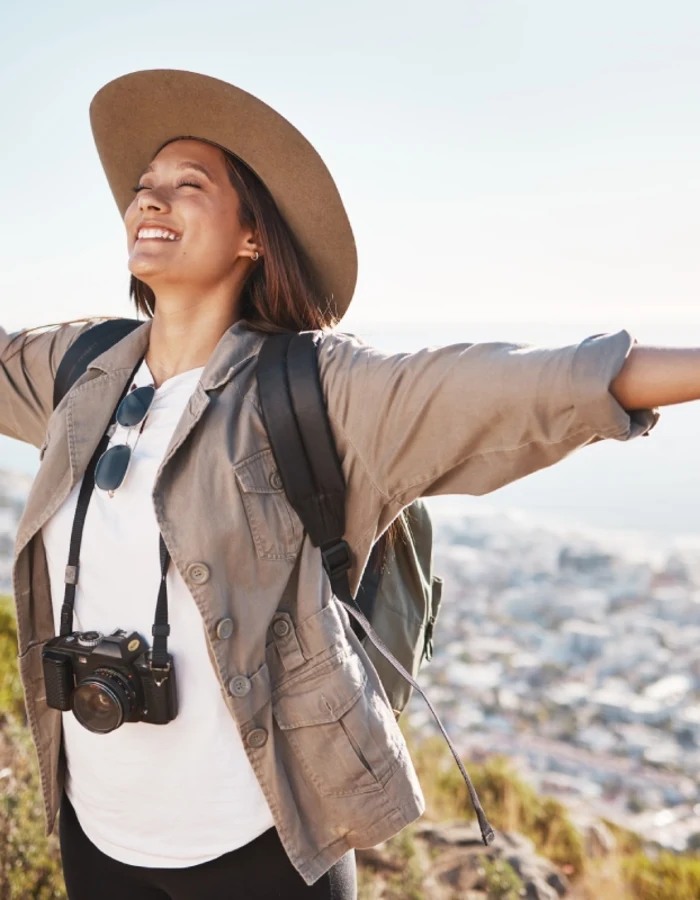 Traveler standing on hillside, arms outstretched, overlooking coastal city and ocean.