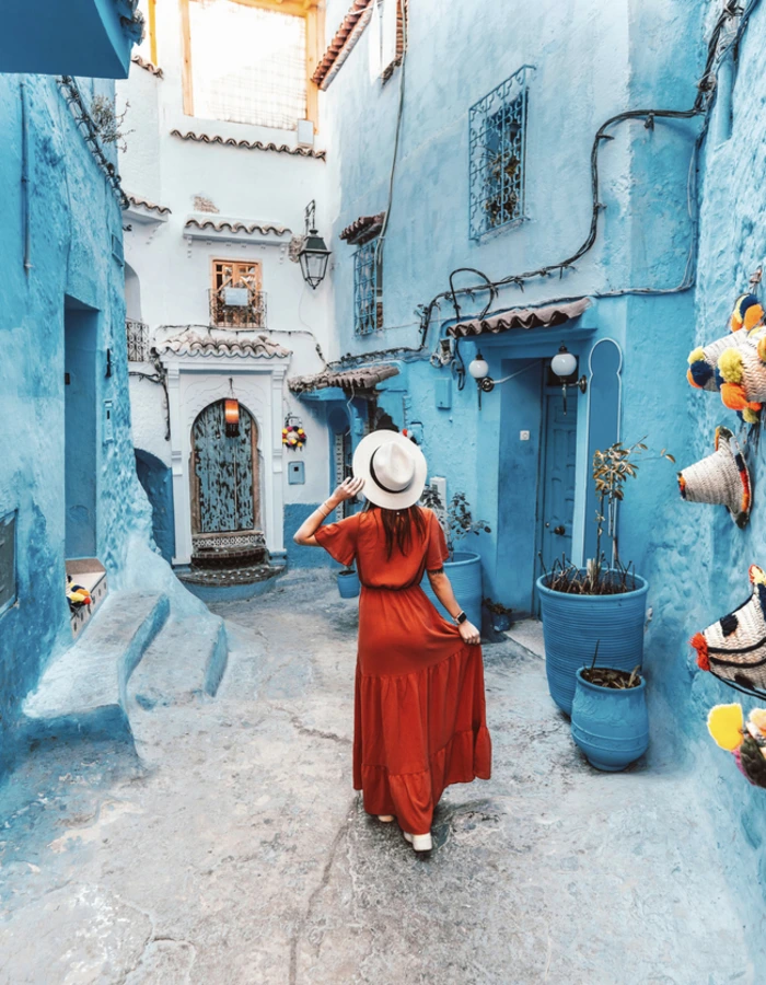 Young woman with red dress visiting the blue city Chefchaouen, Marocco - Happy tourist walking in Moroccan city street - Travel and vacation lifestyle concept