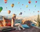 A young woman on a rooftop in Göreme, Cappadocia with hot air balloons in the sky.