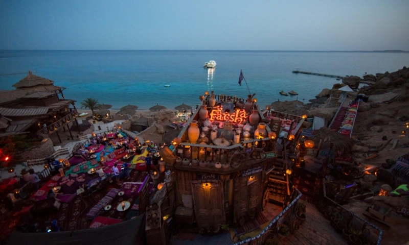 Night view of illuminated Farsha Cafe on cliff overlooking the Red Sea with glowing lanterns, Sharm City