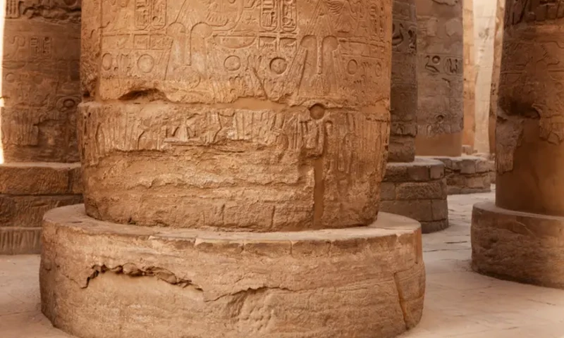 Carved stone columns with hieroglyphic inscriptions and reliefs at the Karnak complex.