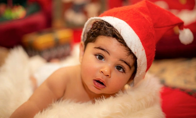 Cute baby boy with curly hair wearing Santa hat lying on white faux fur during Christmas, Christmas in Egypt
