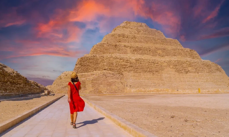 Una joven turista con un vestido rojo en la Pirámide Escalonada de Zoser al atardecer, Saqqara,  El Cairo Egipto