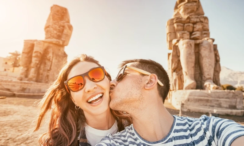 Happy traveler couple in love takes a selfie photo near the famous colossi of Memnon pharaoh statues in Luxor during the honeymoon, Honeymoon in Egypt
