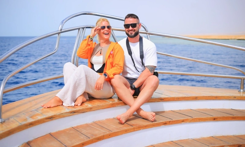 Smiling couple of tourists in sunglasses and casual summer clothes relaxing on the wooden deck of a yacht, Honeymoon in Egypt
