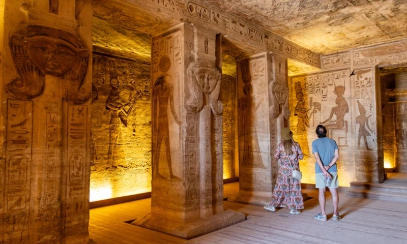 Visitors observing ancient egyptian hieroglyphs inside the temple of hathor at abu simbel, Egyptian Deities