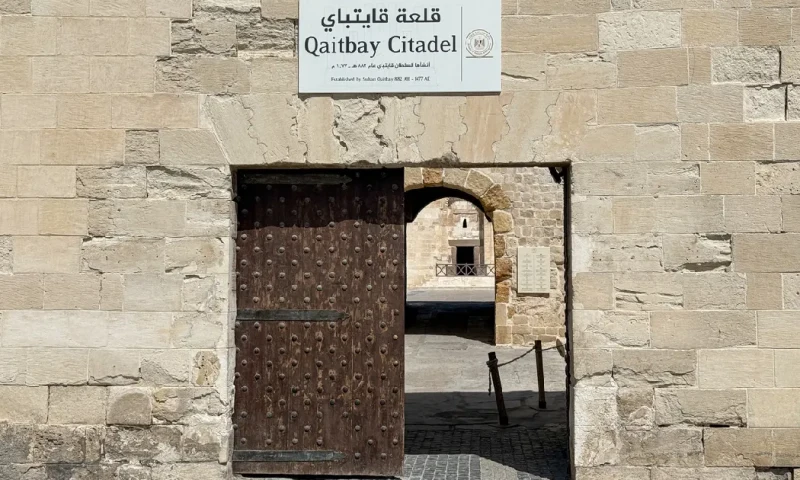 Puerta de entrada de la Ciudadela de Qaitbay con un cartel oficial sobre el muro histórico de piedra, Ciudadela de Qaitbay