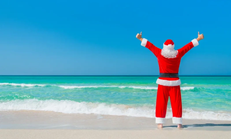 Papá Noel en una playa tropical, con los brazos levantados, disfrutando de sus vacaciones, navidad en egipto