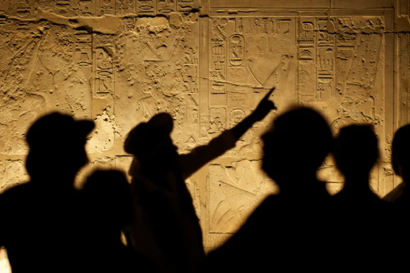 Los jeroglíficos egipcios forman un fondo interesante para la silueta de un grupo de arqueólogos turistas.