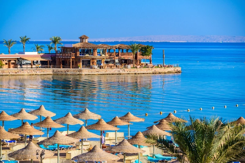 Playa de Hurghada con sombrillas y resort frente a las aguas tranquilas del mar Rojo.