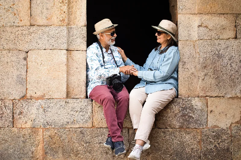 Pareja mayor sentada en una ventana de un Templo Antiguo, sonriendo y tomados de la mano durante un viaje