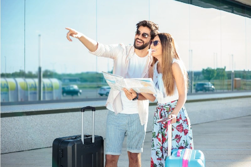 Pareja de viajeros consultando un mapa en el aeropuerto junto a su equipaje.