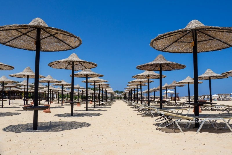 Sombrillas y tumbonas en una playa de Marsa Matrouh con arena blanca y cielo azul.