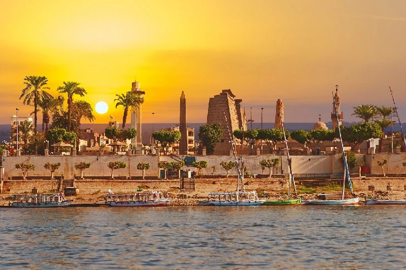 Vista del Templo de Luxor al atardecer desde un crucero por el río Nilo, felucas navegando frente a uno de los monumentos más emblemáticos de Egipto.