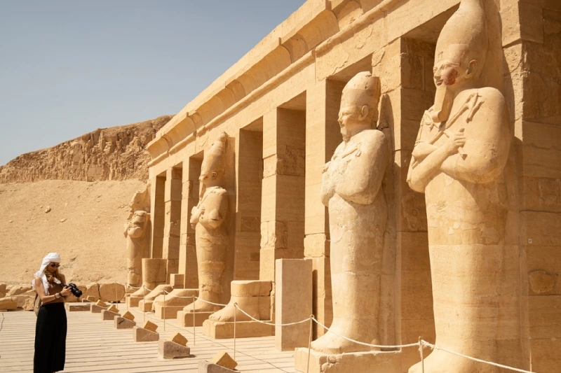 Una mujer turista enfrente de las estatuas del Templo de Hatshepsut en Egipto