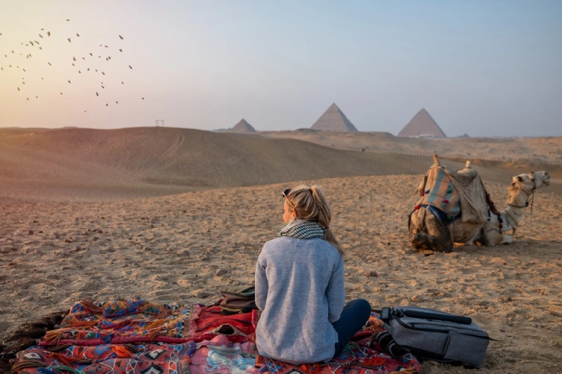 una mujer turista sentando enfrente a las Pirámides de Giza