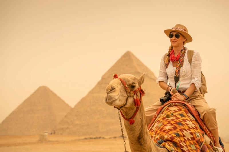 Turista de vacaciones montando camellos frente a las pirámides. Egipto, El Cairo - Guiza.