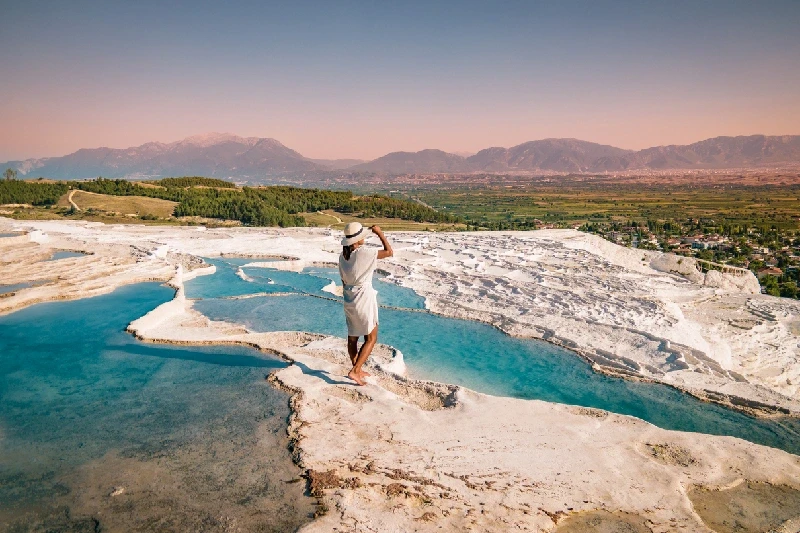 A woman in a white dress standing on the travertine terraces of Pamukkale.