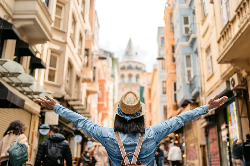A girl stands with her arms raised in front of the Galata Tower in Istanbul.