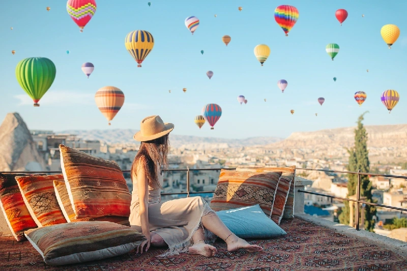 A young woman on a rooftop in Göreme, Cappadocia with hot air balloons in the sky.