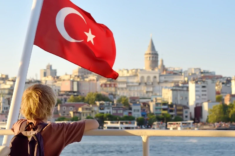 A boy enjoying a Bosphorus cruise with the Turkish flag waving beside him.