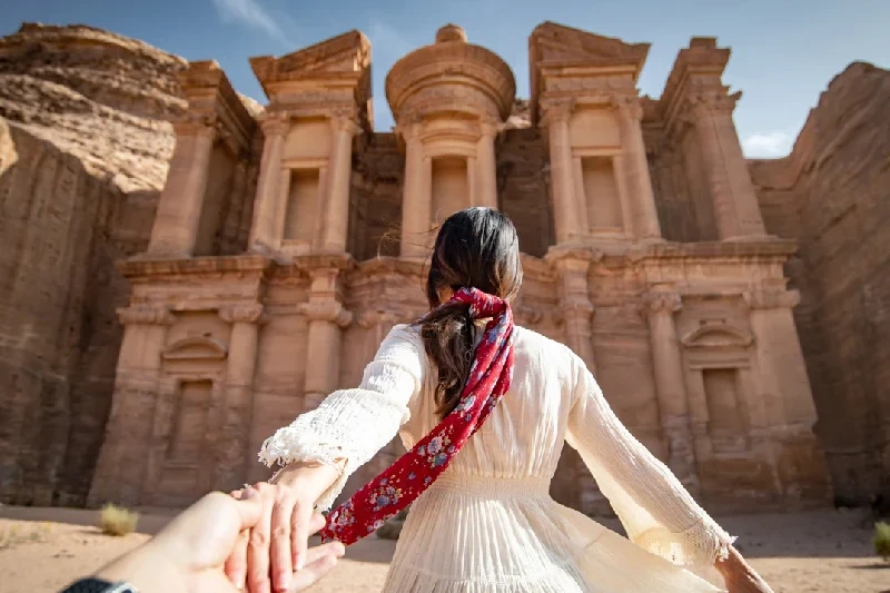 A woman in a white dress holding her partner’s hand at Ad Deir, Petra, Jordan.