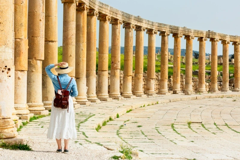 Traveler in a bright dress and hat admiring Jerash’s South Gate.