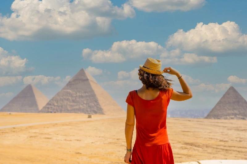 A tourist woman in a red dress gazing at the Great Giza Pyramids.