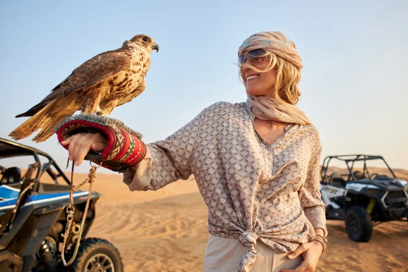 A traveler posing with a majestic falcon in the Dubai desert.