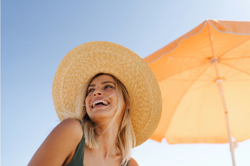 Mujer Sonriente en la Playa llevando un Sombrero de Paja